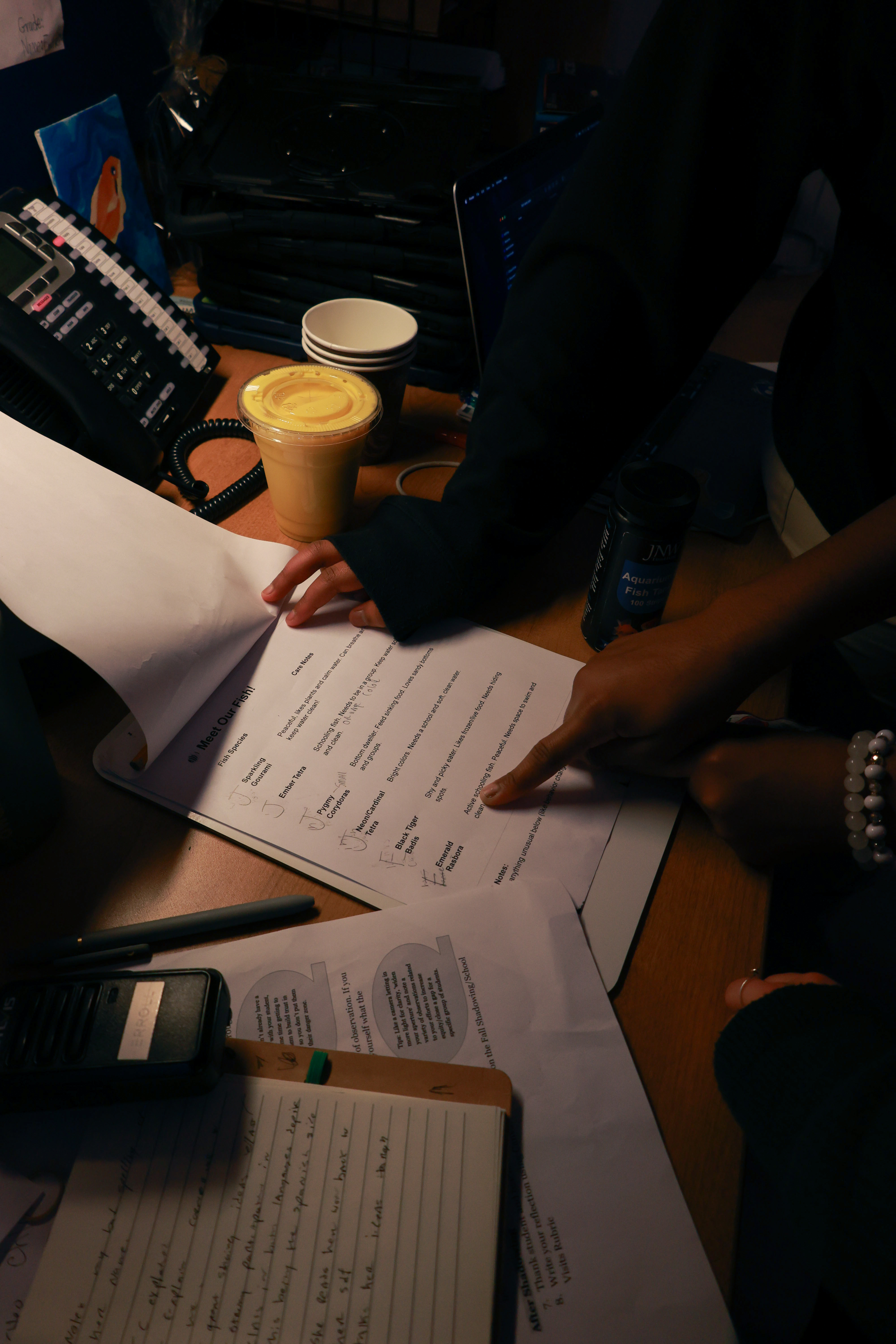 A table covered in papers. A hand points at a bullet point on a to-do list.